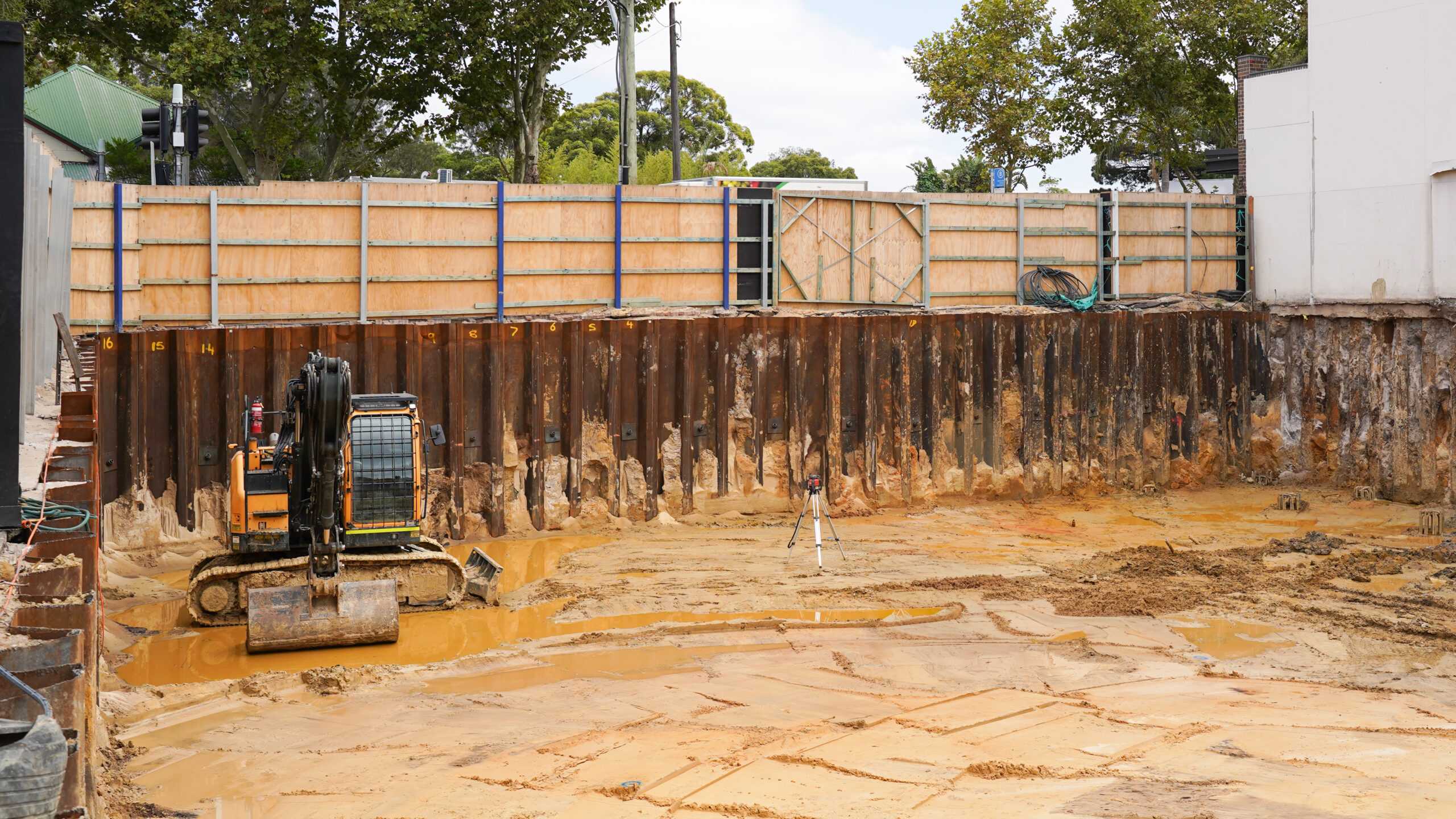 Excavated construction site at 1449-1453 Botany Rd showing sheet pile shoring walls and mini excavator on site.